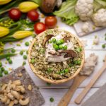 Egészséges vegán salátatál zöldborsóval, karfiollal, gombával és kesudióval, virágokkal és zöldségekkel díszített háttérben