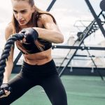 Fiatal nő intenzív kötéles edzést végez szabadtéri fitneszparkban, fekete edzőruhában